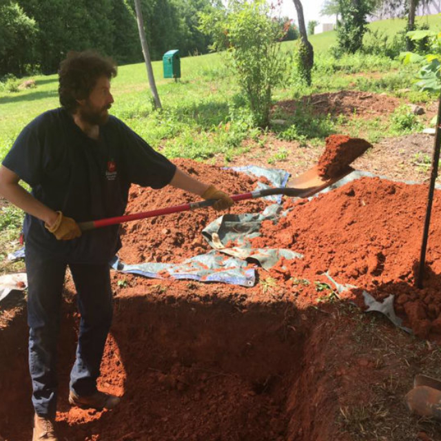 Anthony standing in a grave of red clay, shoveling dirt out.