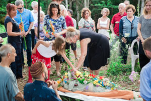 Family and friends gathered around a body at graveside that is covered in a shroud with blowers all around it.