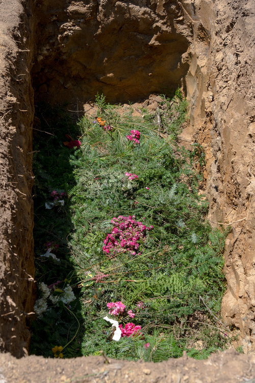 Close up of Paulu's grave showing pine branches and flowers at the bottom.