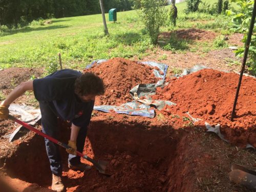 Anthony digging a grave, piles of red clay around him.