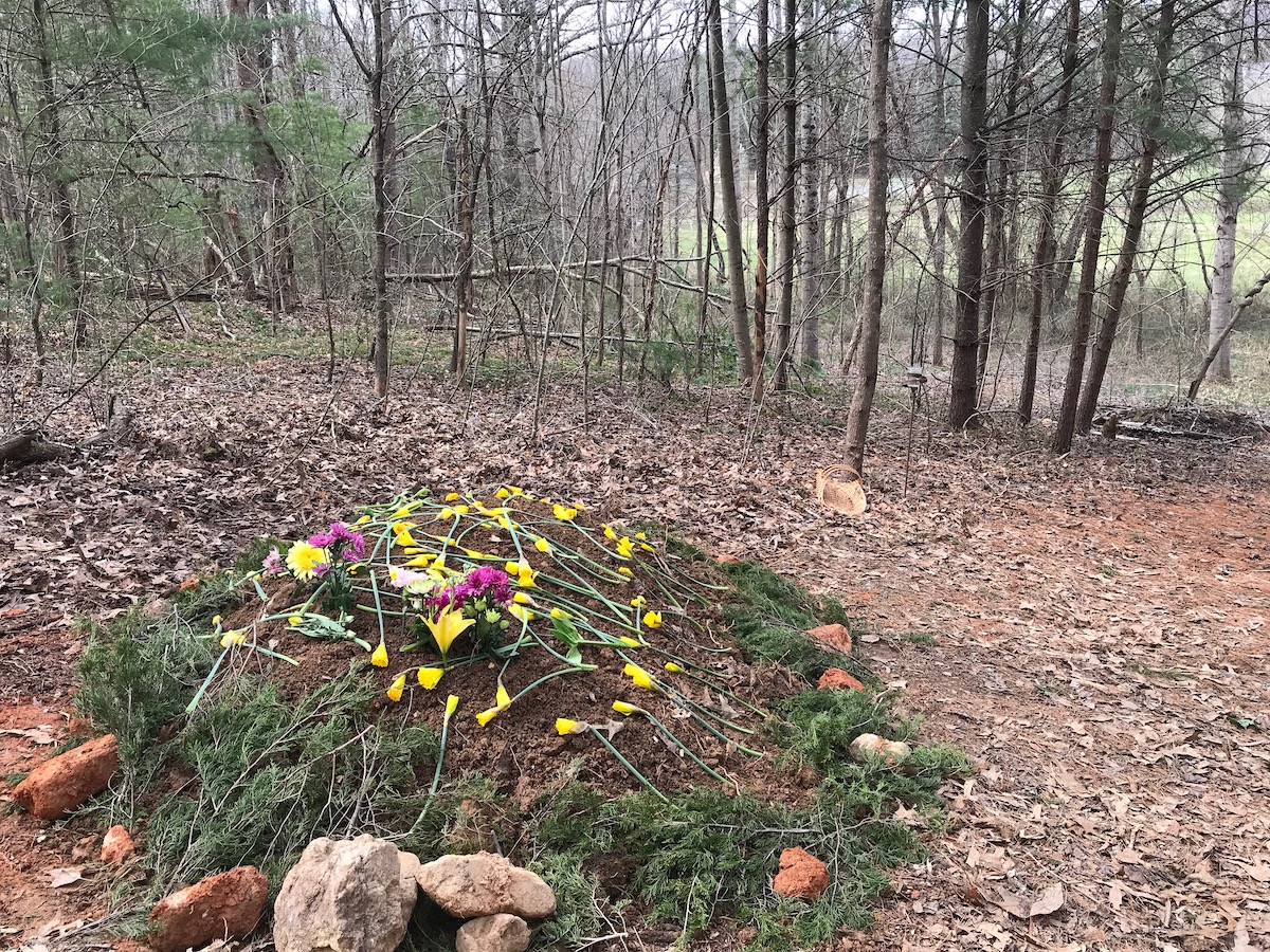 a grave surrounded with rocks and pine bows with yellow and pink flowers on top