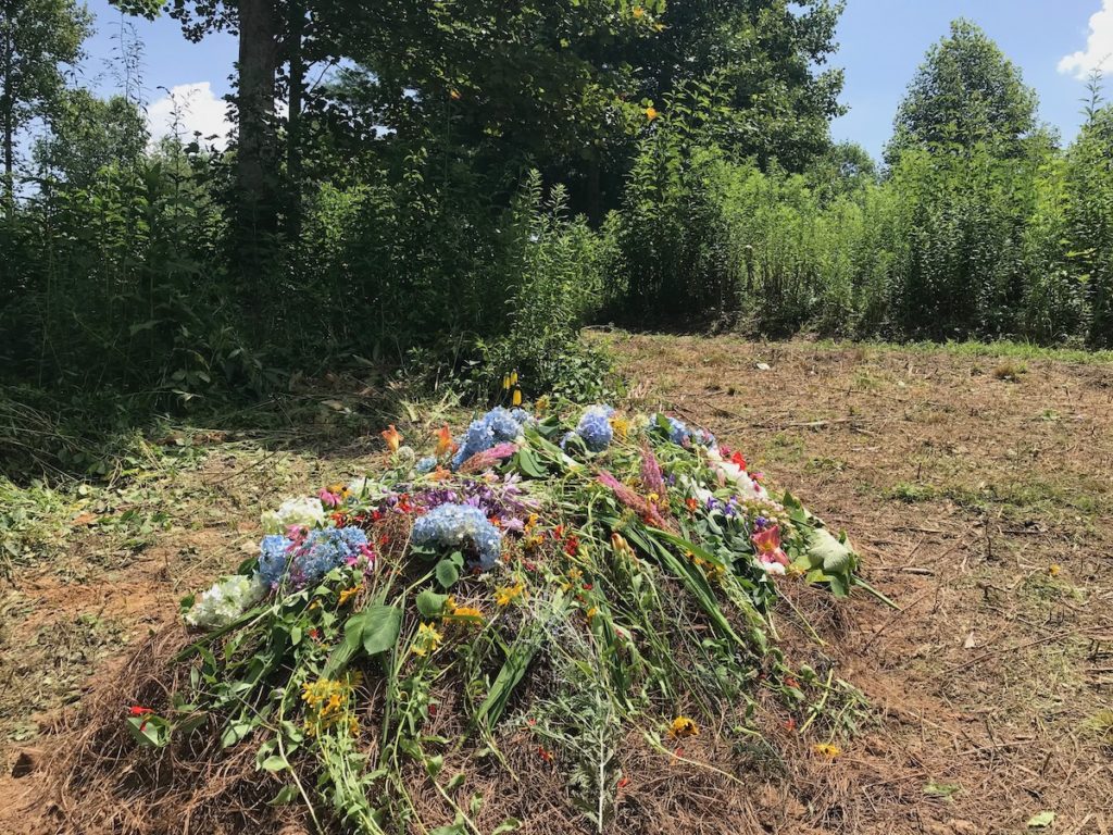 grave covered in different color flowers with plantlife in the background