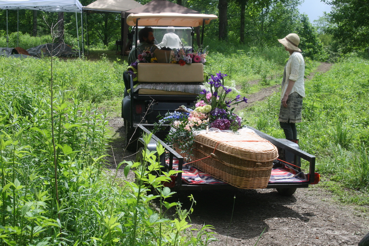 woven casket on top of a trailer being pulled by a golf cart through a meadow