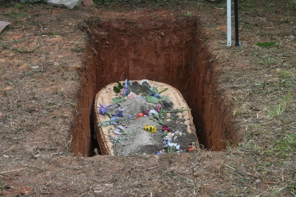 woven casket in a grave with flowers and earth on top of it