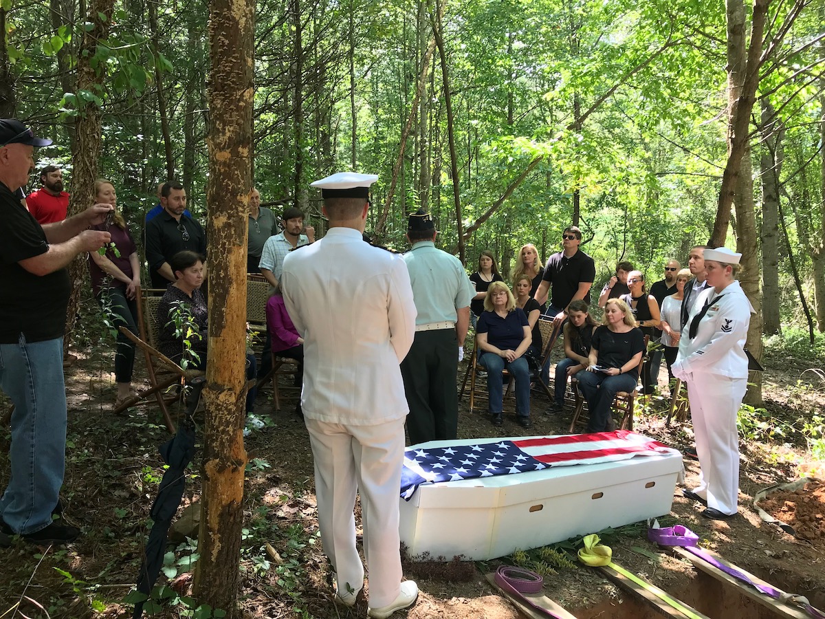 a cardboard coffin covered with an american flag and two military service people