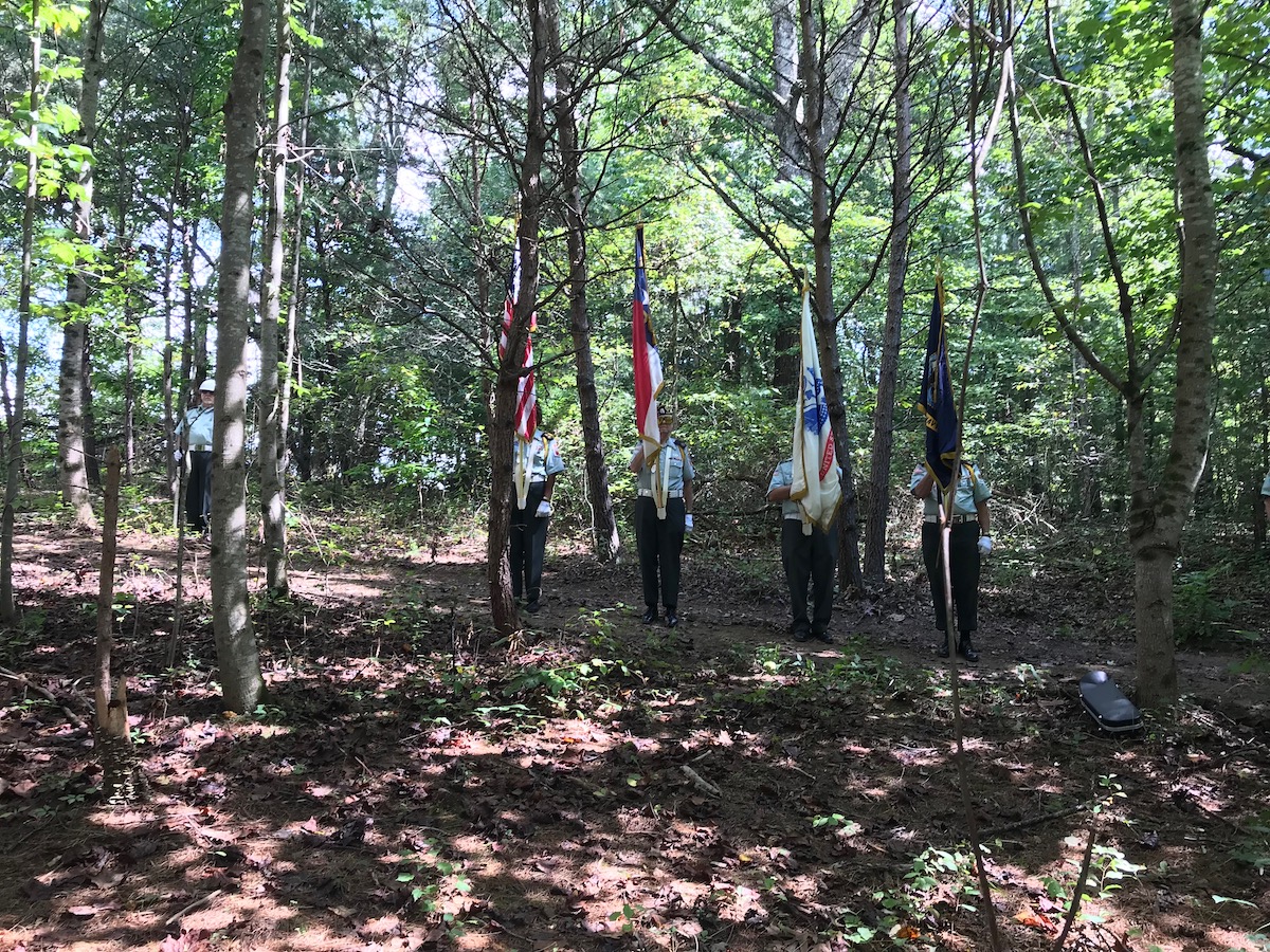 4 men holding flags during military honors in a stand of trees